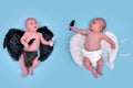 A newborn baby boy with white angel wings and a child with black evil wings, blue studio background