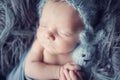 Newborn baby boy  wrapped in blue wrap on gray furry blanketwith knitted toy in hand and with blue woolen cap on head Royalty Free Stock Photo