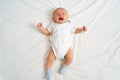 a newborn baby cries on a white sheet. childish tantrums. top view.