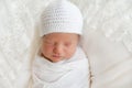 Newborn baby 7 days wrapped in white diaper and hat and sleeping