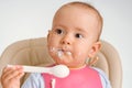 A newborn baby with a dirty face eats cottage cheese with a spoon on his own, portrait close up