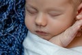 Newborn - baby, face close-up. The sleeping Newborn boy under a white knitted blanket lies on the blue fur. Royalty Free Stock Photo