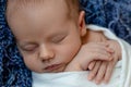 Newborn - baby, face close-up. The sleeping Newborn boy under a white knitted blanket lies on the blue fur. Royalty Free Stock Photo