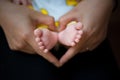 Newborn baby feet on female hands shape like lovely heart