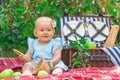 Newborn baby girl in a blue dress on a picnic. A 9-12 month toddler with an empty basket and green apples around Royalty Free Stock Photo