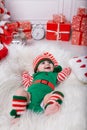 Newborn baby girl dressed in gnome costume lying on white fur carpet among christmas decorations. Royalty Free Stock Photo