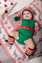 Newborn baby girl dressed in gnome costume lying on white fur carpet among christmas decorations. Royalty Free Stock Photo