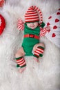 Newborn baby girl dressed in gnome costume lying on white fur carpet among christmas decorations. Royalty Free Stock Photo
