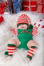 Newborn baby girl dressed in gnome costume lying on white fur carpet among christmas decorations. Royalty Free Stock Photo