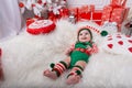 Newborn baby girl dressed in gnome costume lying on white fur carpet among christmas decorations. Royalty Free Stock Photo