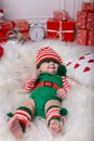 Newborn baby girl dressed in gnome costume lying on white fur carpet among christmas decorations. Royalty Free Stock Photo