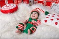 Newborn baby girl dressed in gnome costume lying on white fur carpet among christmas decorations. Royalty Free Stock Photo