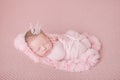 Newborn baby girl in a pink cocoon on a pink background, sleeping princess with a crown Royalty Free Stock Photo