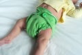 Newborn baby in green reusable diaper on a white sheet. Modern eco friendly cloth nappy for infant child hygiene. Sustainable