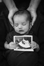 newborn baby holding ultrasound copy in hand and sleeping at mother palm in black and white Royalty Free Stock Photo