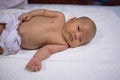 Newborn baby is laying on the white bed. New born is no hair. Child is 1 months. Asian Infant is wearing white fabric diaper.