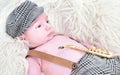 a newborn baby is lying on a white fur in a cap and with a guitar Royalty Free Stock Photo