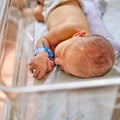 A newborn baby with a maternity hospital bracelet on his arm is sleeping in a crib. A newly born child in a clinic bed behind a Royalty Free Stock Photo