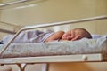 A newborn baby with a maternity hospital bracelet on his arm is sleeping in a crib. A newly born child in a clinic bed behind a Royalty Free Stock Photo