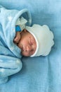 Newborn Baby Red Cute Face Portrait Early Days Sleeping In Medical Glass Bed On Blue Background. Child At Start Minutes Royalty Free Stock Photo