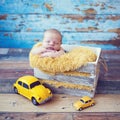 Newborn baby sleeping in vintage box with yellow fur blanket and holding small yellow car toy in hand. Baby boy sleeping with him Royalty Free Stock Photo