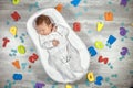 Newborn baby sleeps in a special orthopedic mattress Baby cocoon, on a wooden floor multicolored letters around. Calm Royalty Free Stock Photo