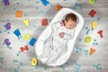 Newborn baby sleeps in a special orthopedic mattress Baby cocoon, on a wooden floor multicolored letters around. Calm Royalty Free Stock Photo