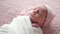 Newborn Baby In Swaddling Blankets And In A Warm Hat Lying On The Bed