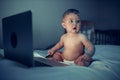 A newborn baby uses a computer while sitting on a sofa at night. The child is dressed in a diaper on his body