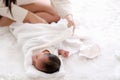 Newborn baby was swaddling with white cloth by her mother and the activity is on bed