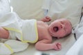 Newborn baby yawns hiding behind his hand. The baby, covered with a white diaper, wakes up. The child blinks yawning. The Royalty Free Stock Photo