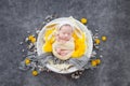 Newborn baby in a yellow cocoon and a white bunny hat sleeps in a white wooden bowl decorated with spring yellow flowers