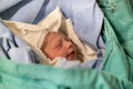 Newborn, eyes closed, crying baby in green blanket in hospital