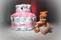 Newborn gift concept. Cake of diapers. Wrapped diapers as cake with flowers. Cake of wrapped clean diaper on table with baby doll