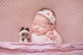 Newborn girl in a cocoon sleeps in a pink bed with a Siamese toy cat