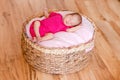 Newborn girl in pink bodysuit barefoot lies in round crib and sleeps