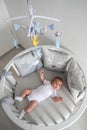 Newborn lies in the round white bed with mobile