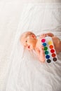 Newborn with paints on a white plaid closeup. Infant holds watercolor rainbow paint and copy space. The concept of the game, care