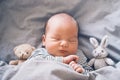 Newborn sleep at first days of life. Portrait of new born baby one week old with cute soft toy in crib in cloth background