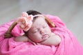 Newborn sleeping with knitted flower on head. Infant baby girl lying on pink blanket in basket. Cute portrait of child. Royalty Free Stock Photo