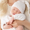 Newborn sleeping in Mother Arms. Sleepy Baby Portrait in Hat. Mom Hand on little Child Stomach. Cute Baby Gnome in White Cap