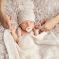 Newborn sucking Pacifier in Sleep. Parent holding Baby Fist in Hands. One Month little Child with Dummy in knitted Hat covered Royalty Free Stock Photo