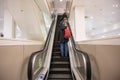 People on escalator inside modern building. Man with red bag