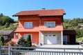 Newly built suburban family house with pink facade and stone tiles covered garage surrounded with decorative plants and trees