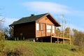 Newly built wooden mountain cabin with front porch and new roof on top of small hill surrounded with grass and trees Royalty Free Stock Photo