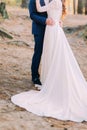 Newly married couple holding each other. Bride's long dress tail spreading on the sand Royalty Free Stock Photo