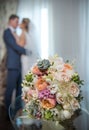 Newly-married couple kissing and wedding bouquet in the foreground. Royalty Free Stock Photo