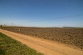 Newly Ploughed Field Against Blue Sky Bordered by Dirt Road