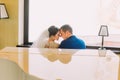 Newlywed bride and groom near the white grand piano going to kiss. Bright window on background Royalty Free Stock Photo