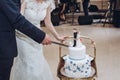 Newlywed couple cutting cake at wedding reception, bride and groom slicing delicious white cake decorated with funny figures of